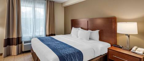 A hotel room with a bed, a bedside table with a lamp, a phone, and a window with curtains.