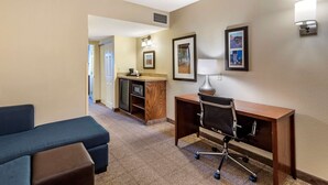 A hotel room with a blue sofa, a wooden desk, a chair, a small kitchenette, and framed pictures on the wall. - Comfort Inn & Suites Virginia Beach - Norfolk Airport (Virginia Beach)