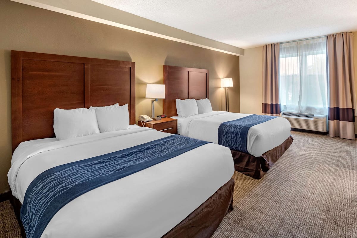 Habitación de hotel con dos camas, una mesita de noche con teléfono, lámpara y ventana con cortinas.