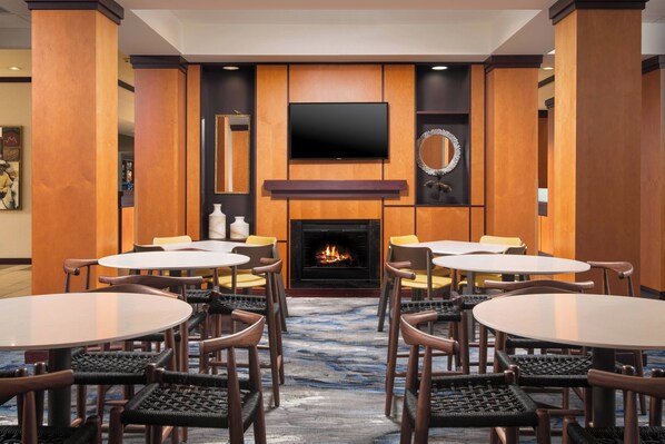 Un vestíbulo de hotel con chimenea, televisor de pantalla plana y varias mesas y sillas redondas.