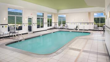 Una piscina con sillas y una tumbona, ventanas amplias y vistas a las colinas.