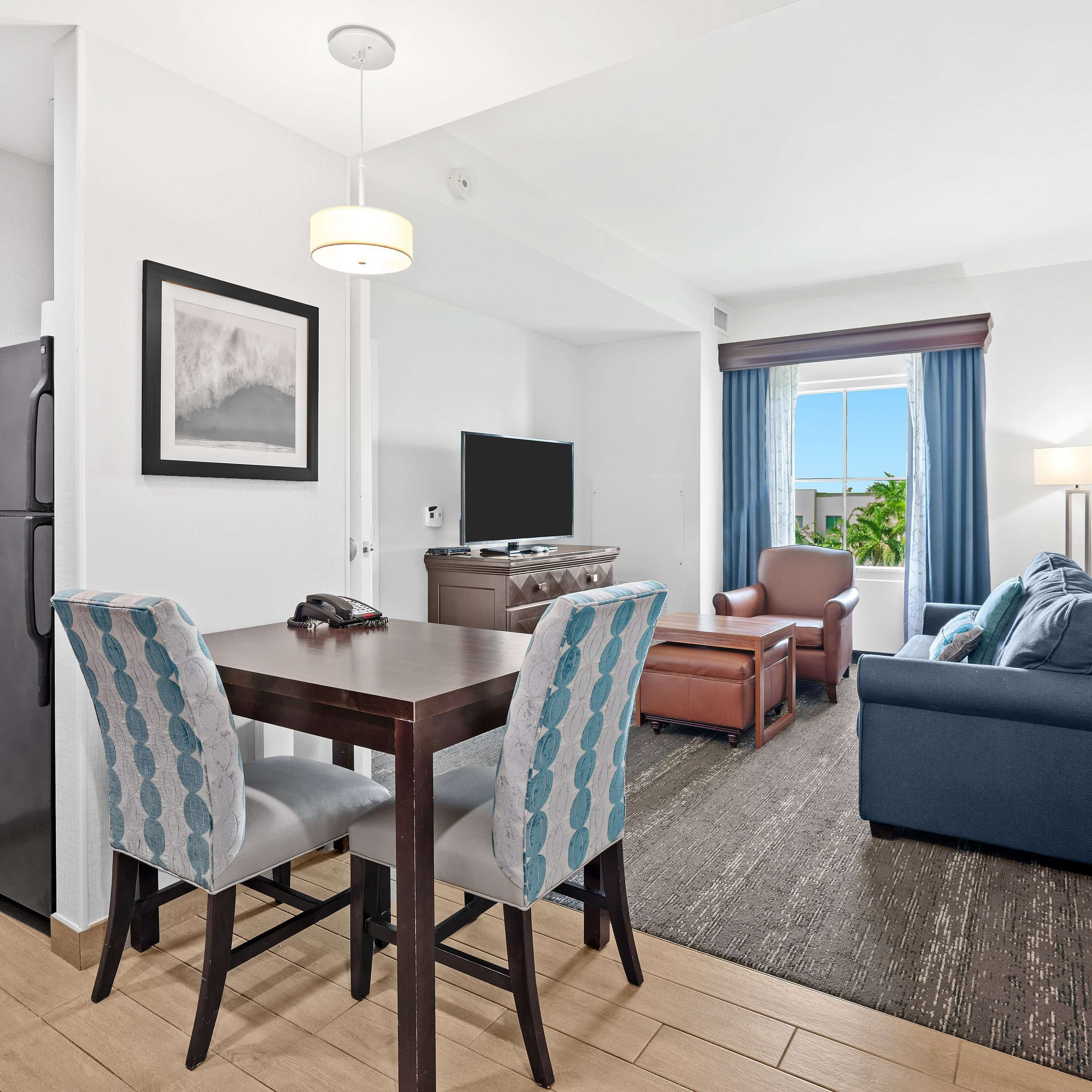 Habitació d'hotel moderna amb zona de dinar, saló i finestra gran amb cortines.