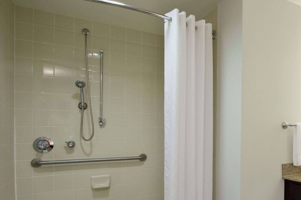 Un bagno con doccia, barra di sostegno e lavandino bianco.