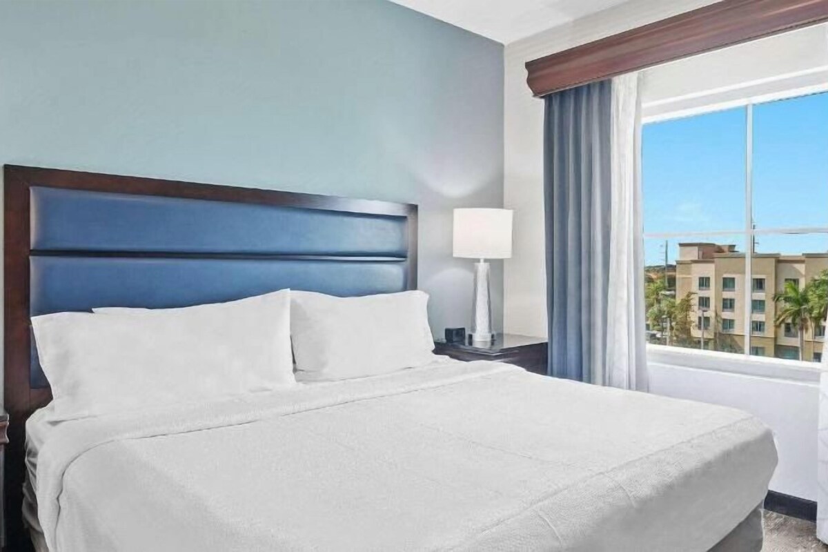 A hotel room with a large bed, a nightstand, a lamp, and a window with curtains.
