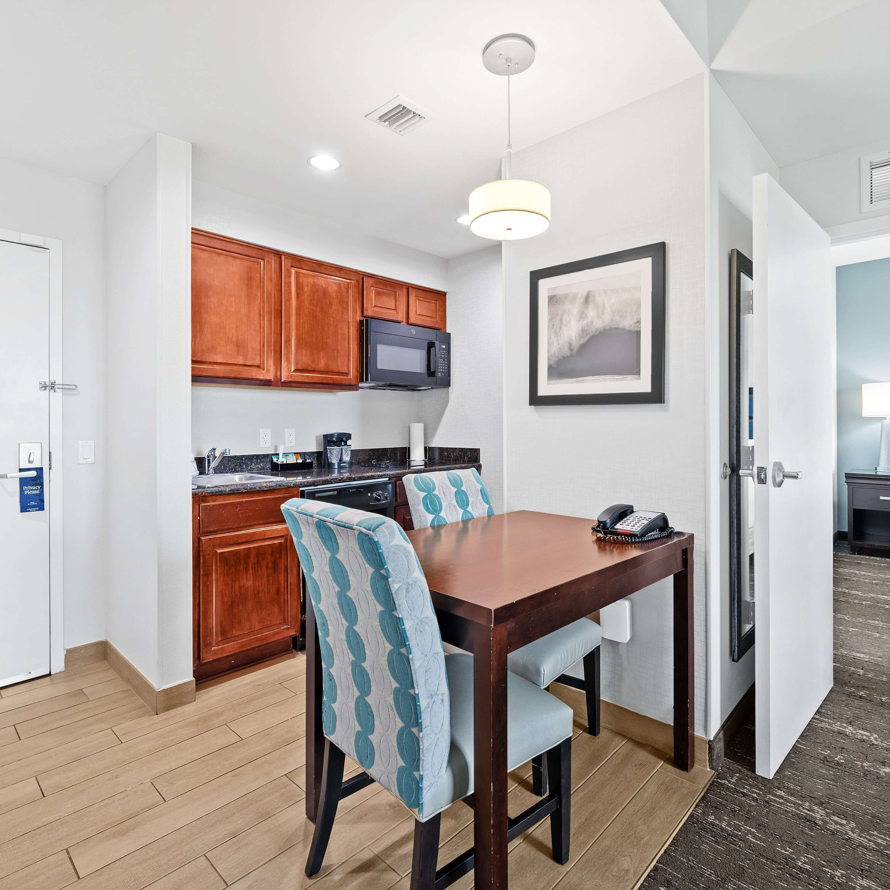 A modern kitchen with wooden cabinets, a built-in microwave, and a dining area with a wooden table and patterned chairs.