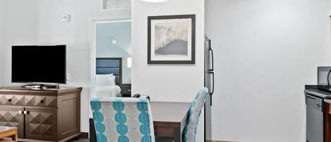 Una sala de estar moderna con un sofá, una mesa de comedor con sillas, un televisor y una zona de cocina con refrigerador.