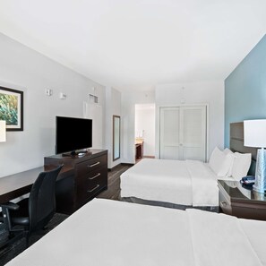 A hotel room with a desk, two beds, a TV, a mirror, and a door.