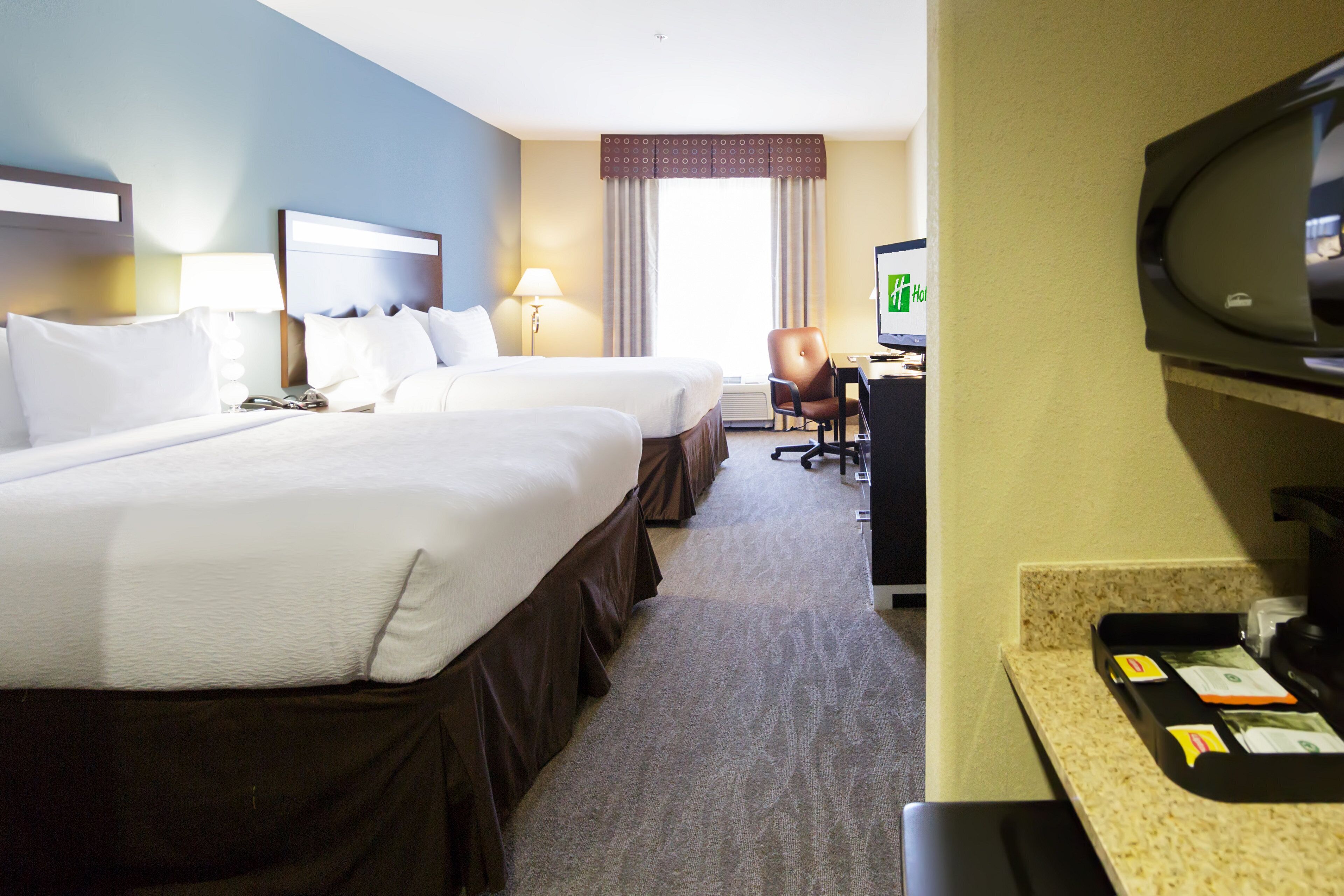 A hotel room with two beds, a desk, a chair, a television, and a minibar.