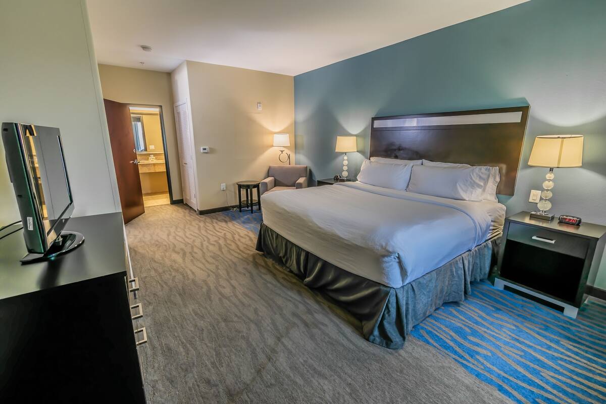 A hotel room with a large bed, bedside tables with lamps, a desk with a computer, and a TV.