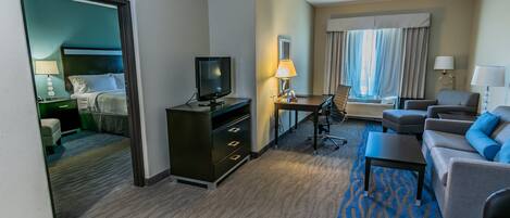 A hotel room with a bed, a desk, a television, a chair, a sofa, and a carpeted floor.