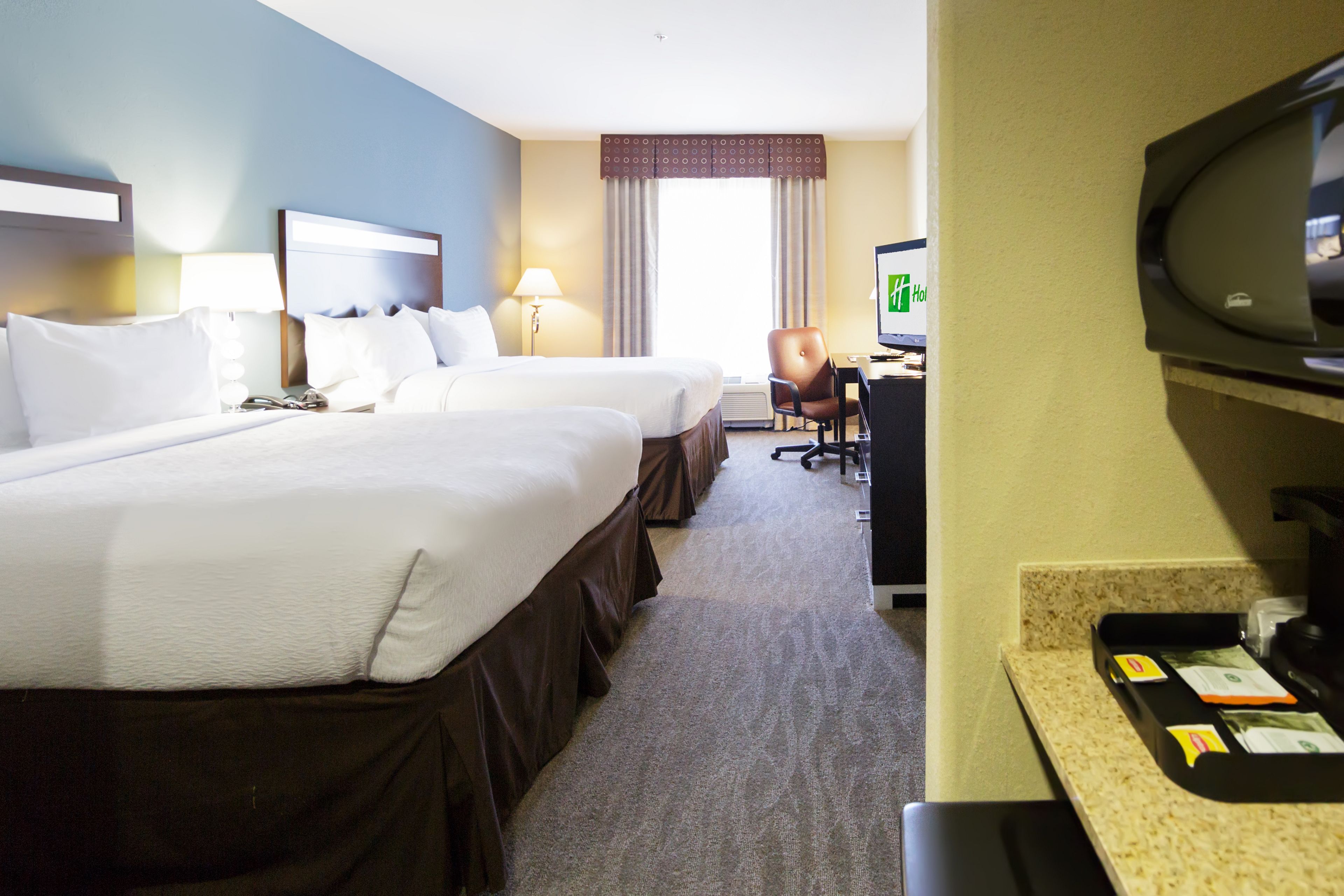 Una habitación de hotel con dos camas, un escritorio con computadora, un televisor y un minibar.