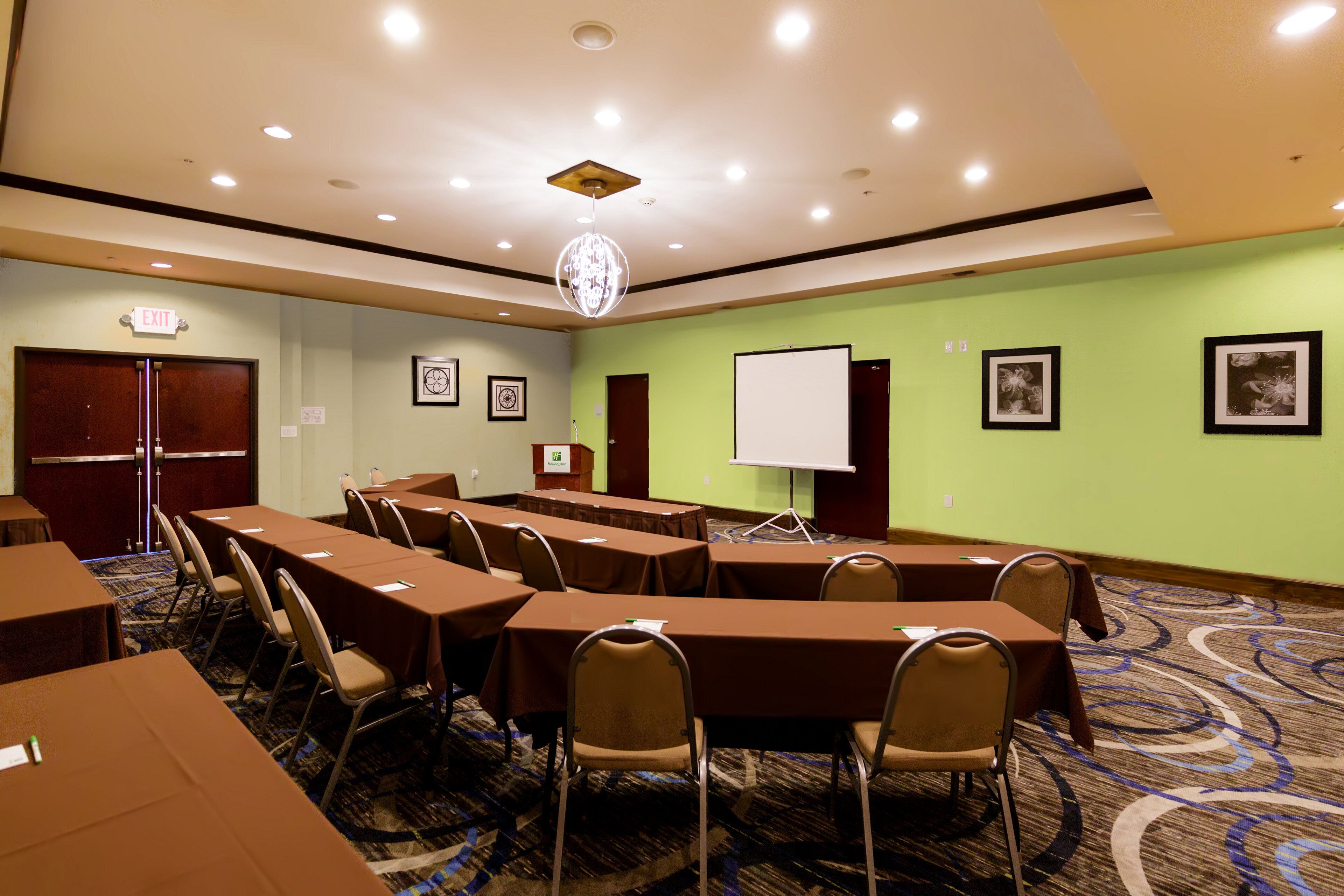 A conference room with tables, chairs, a projector screen, and framed artwork on the walls.
