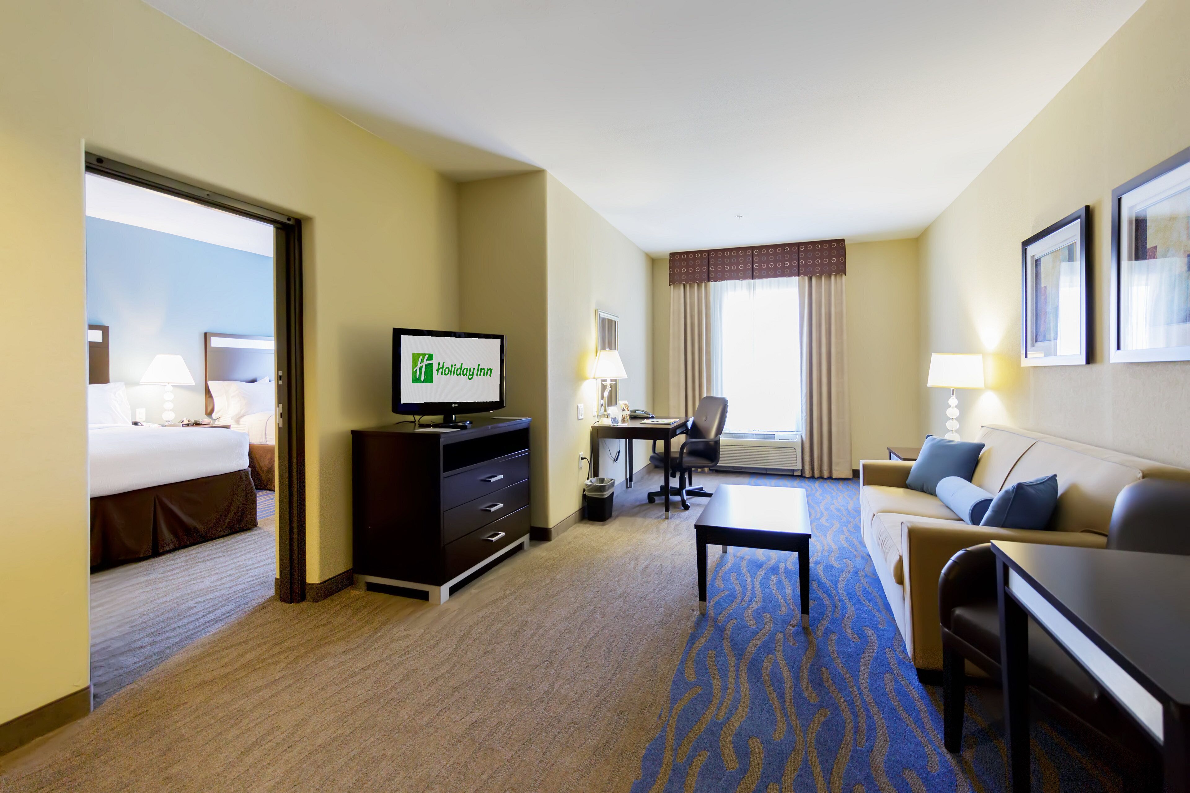 A hotel room with a bed, a desk, a sofa, a television, and a carpeted floor.