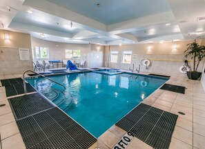 An indoor swimming pool with clear water, a diving board, and a lifeguard chair.