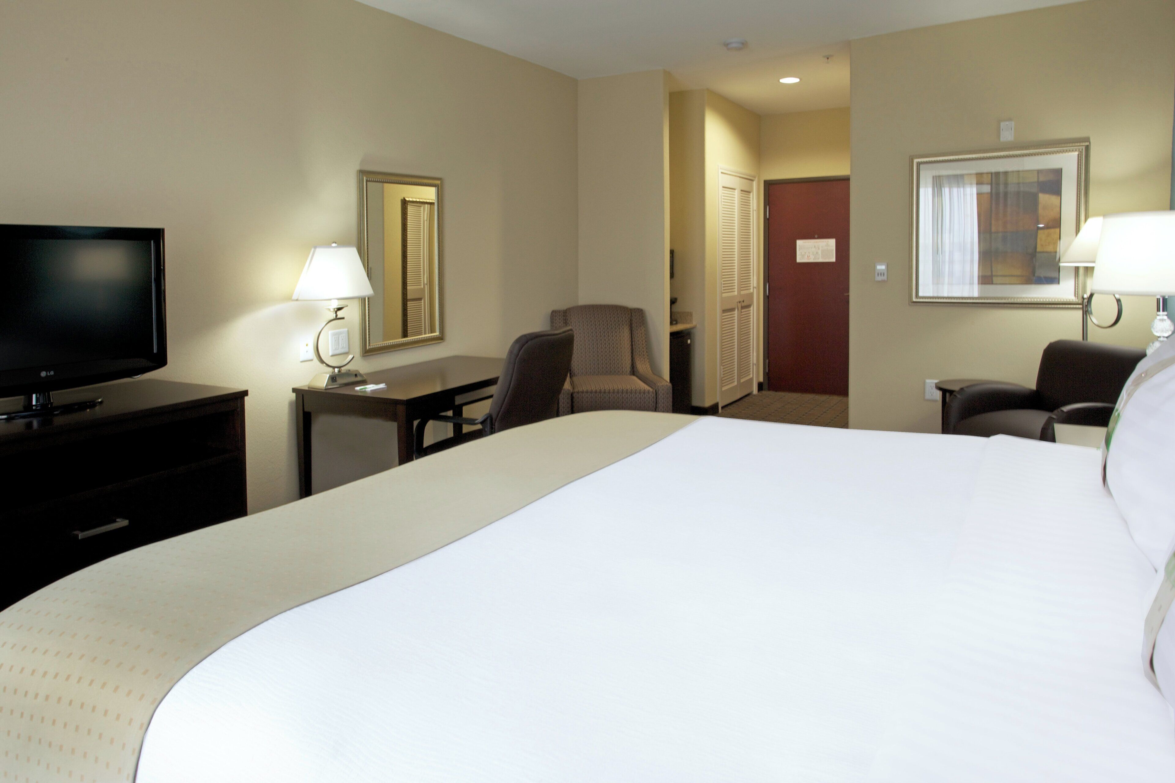 A hotel room with a large bed, a desk, a chair, a television, and two lamps.