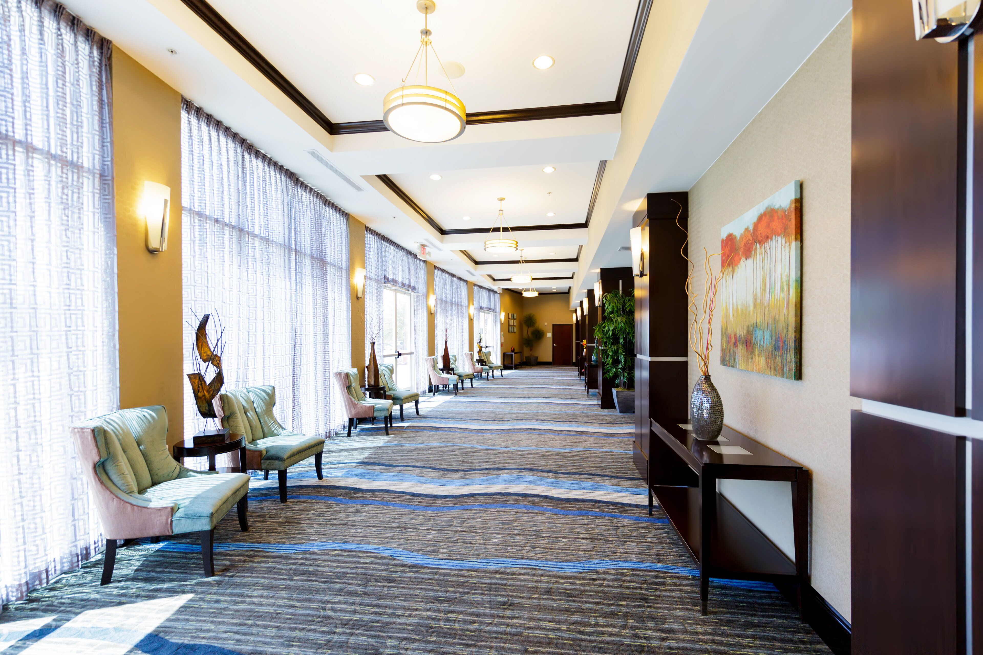 A hotel lobby with a long corridor, seating area with chairs, a carpeted floor, and a painting on the wall.