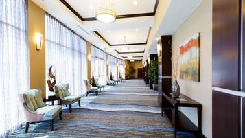 A hotel lobby with a long corridor, seating area with chairs, a carpeted floor, and a painting on the wall.