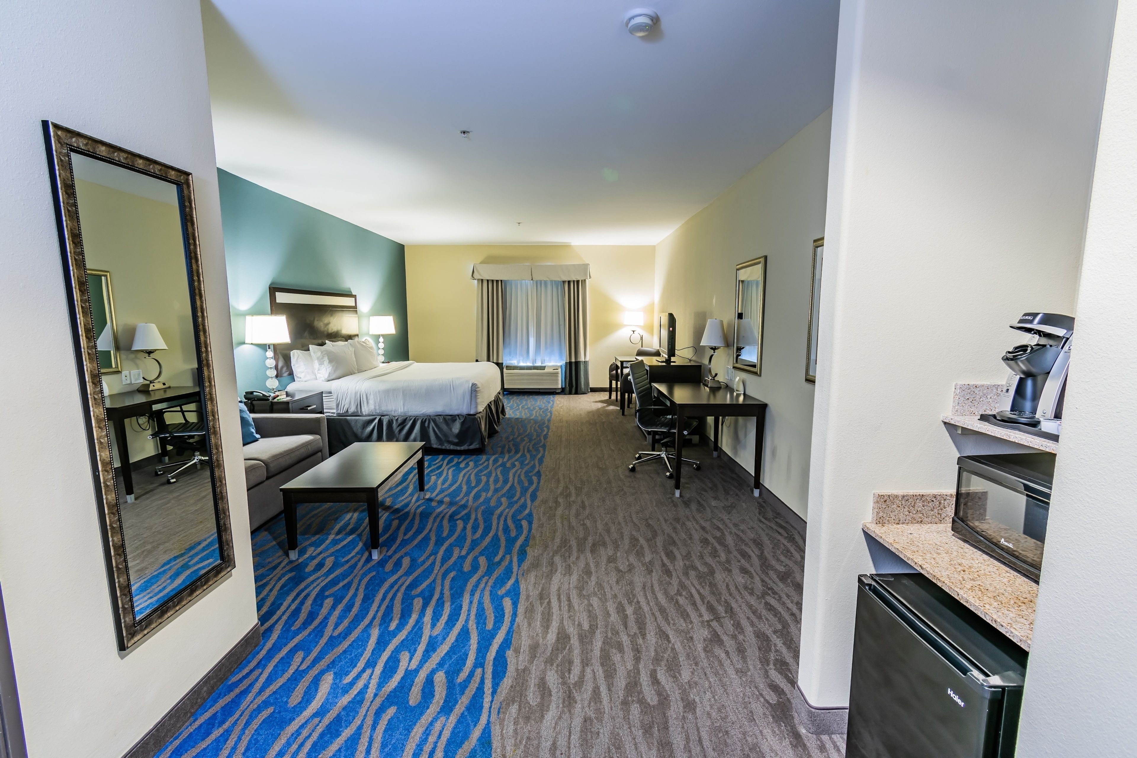 A hotel room with a bed, a desk, a chair, a sofa, a coffee machine, and a microwave.
