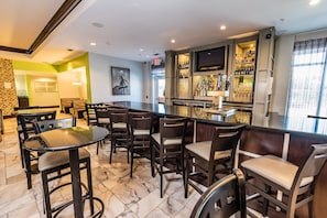 A bar area with multiple seating options, a television, and a variety of bottles and glasses. - Holiday Inn Houston Webster by IHG (Webster)