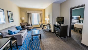 Quarto de hotel com sofá, escrivaninha, televisão e cama.