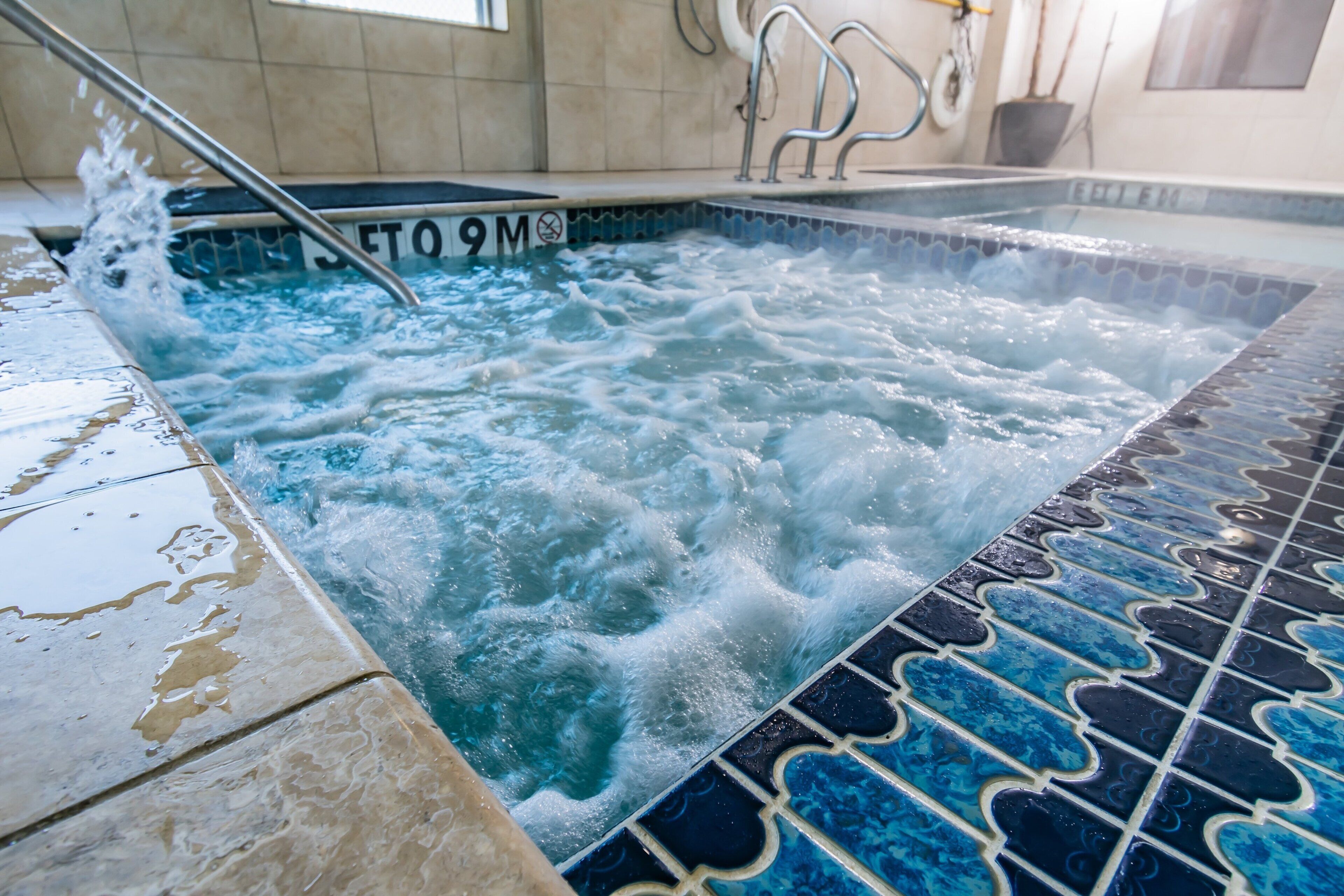 Un jacuzzi con piso de azulejos y escalera metálica.
