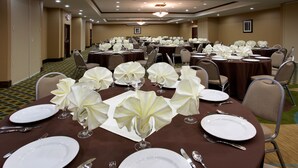 A banquet hall with round tables set for dining, each with white tablecloths, folded napkins, and silverware. - Holiday Inn Houston Webster by IHG (Webster)