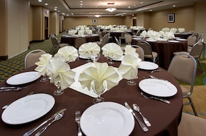 A banquet hall with round tables set for dining, each with white tablecloths, folded napkins, and silverware.