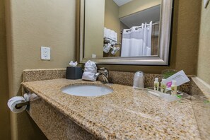 A bathroom with a granite countertop sink, a mirror, a towel rack with white towels, and toiletries. - Holiday Inn Houston Webster by IHG (Webster)