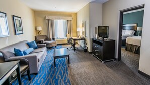 A hotel room with a sofa, armchair, desk, television, and a bed. - Holiday Inn Houston Webster by IHG (Webster)