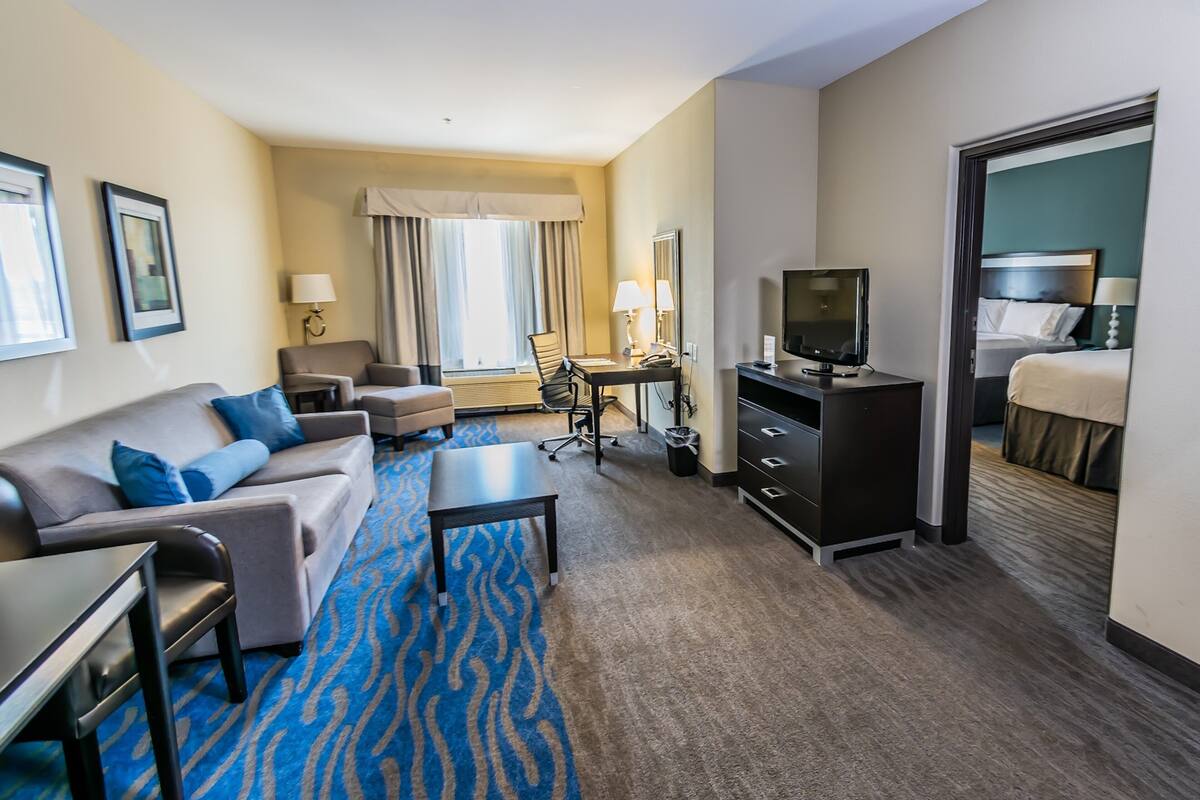 A hotel room with a sofa, armchair, desk, television, and a bed.