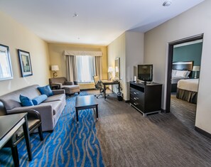 A hotel room with a sofa, armchair, desk, television, and a bed.