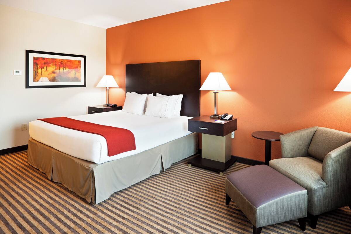 Une chambre d’hôtel avec un grand lit, deux tables de chevet avec des lampes, une chaise et une petite table.