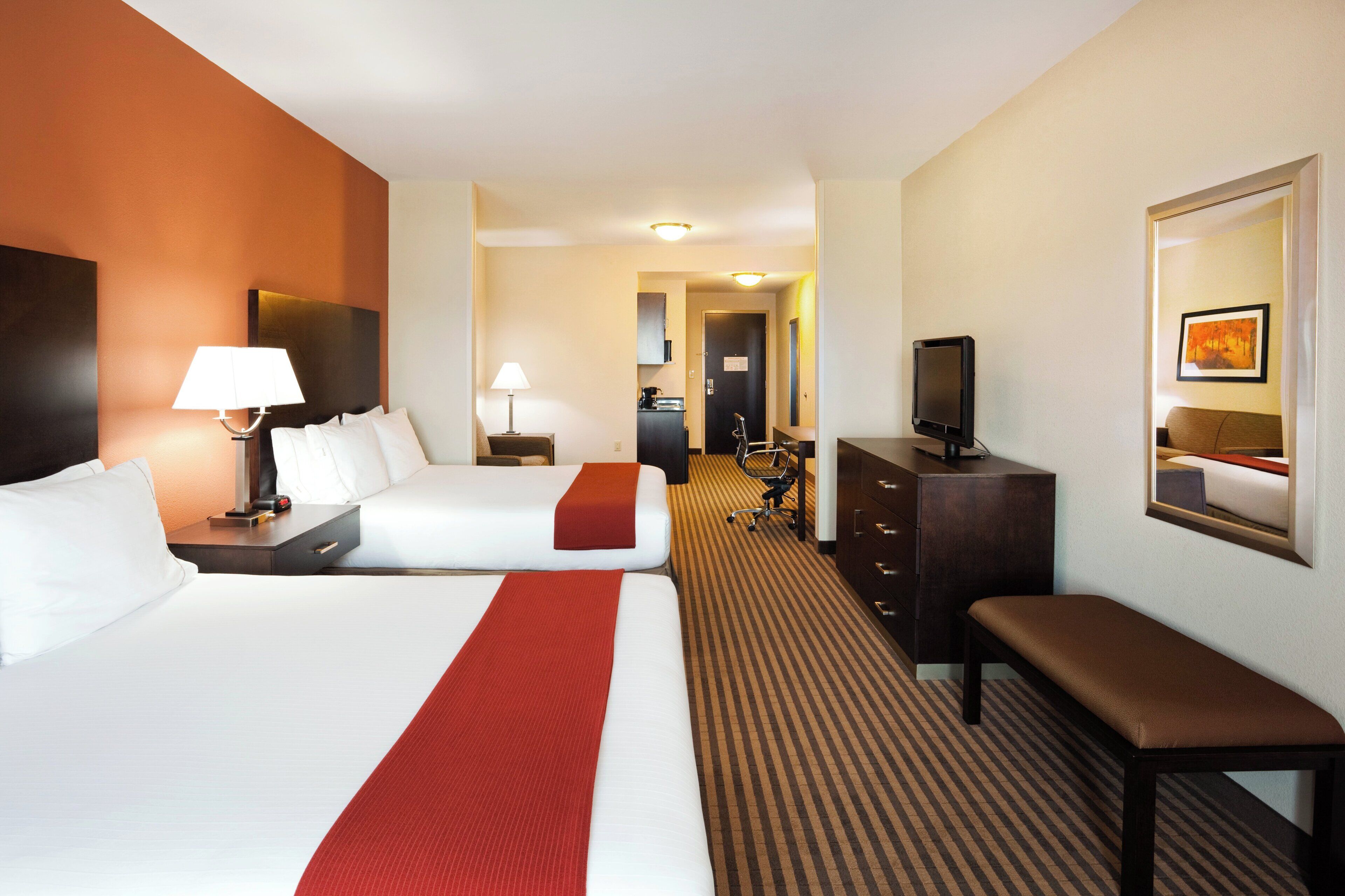 A hotel room with two beds, a desk, a chair, a television, and a mirror.