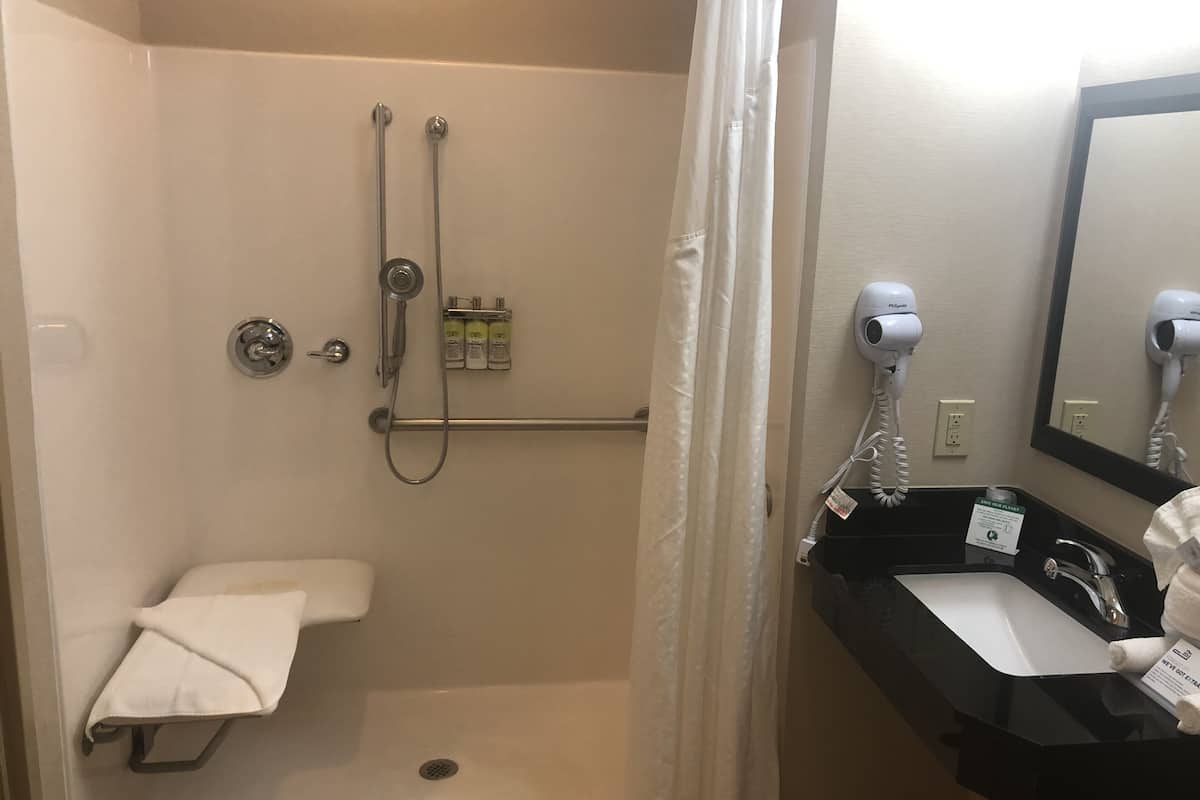 Une salle de bain avec douche, toilettes et lavabo. On y trouve des articles de toilette accrochés au mur, un sèche-cheveux et un porte-serviettes.