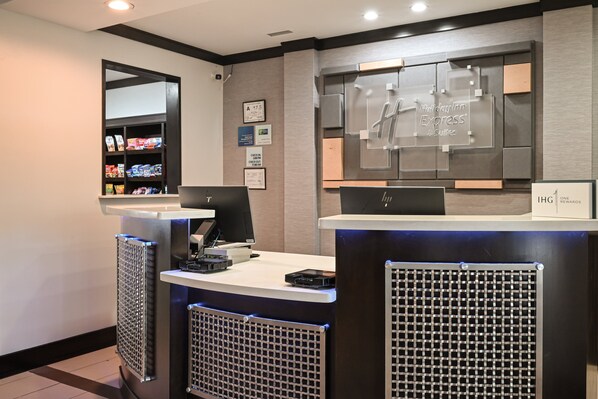 A hotel reception area with a reception desk, computer, and a display of hotel amenities. - Holiday Inn Express & Suites Charlotte Southeast - Matthews by IHG (Matthews)