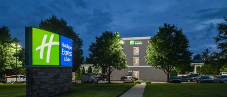 A Holiday Inn Express sign with a stone base, surrounded by well-maintained grass and trees, and a parking lot with several cars.