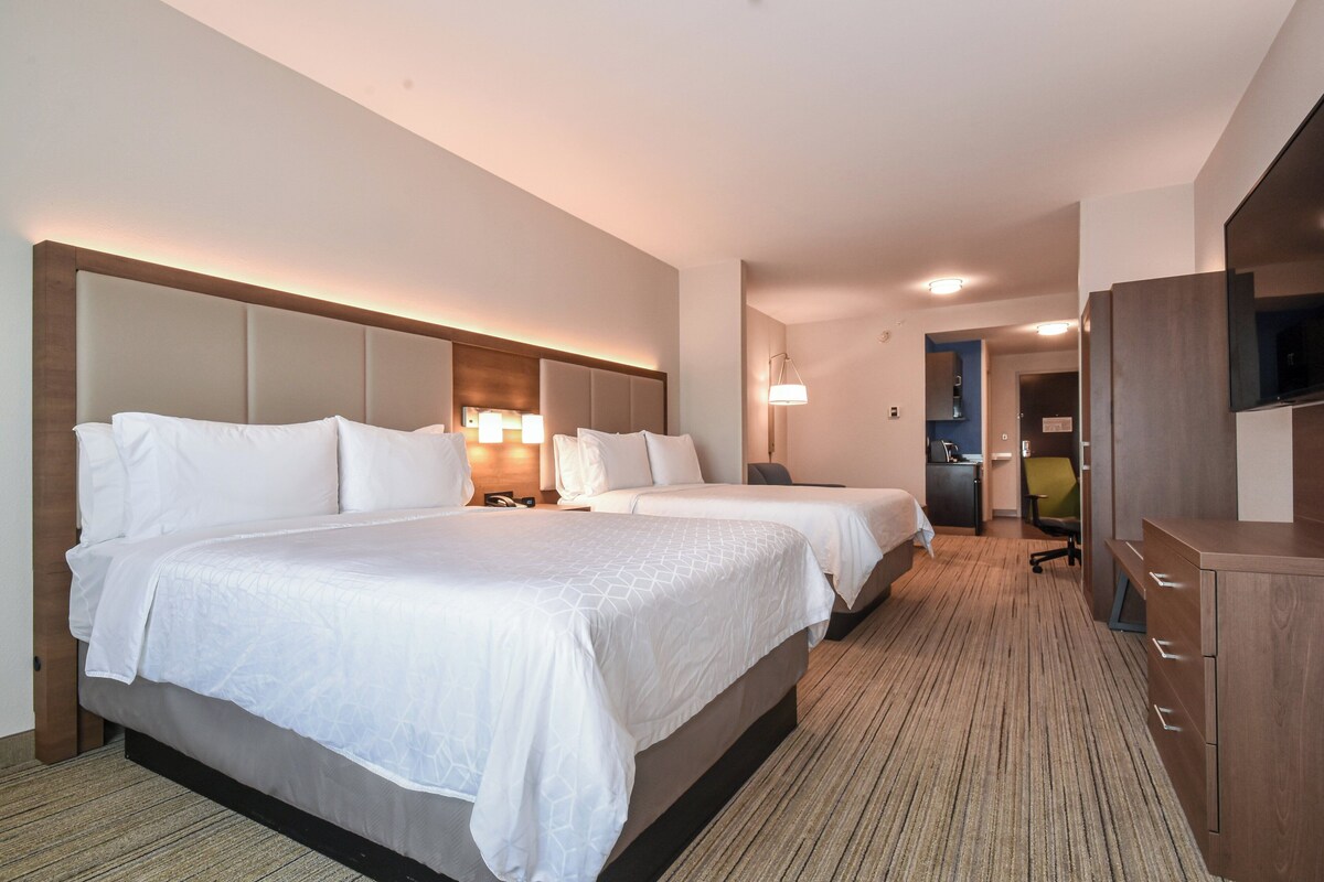 Habitación de hotel con dos camas, un escritorio, una silla y un televisor.