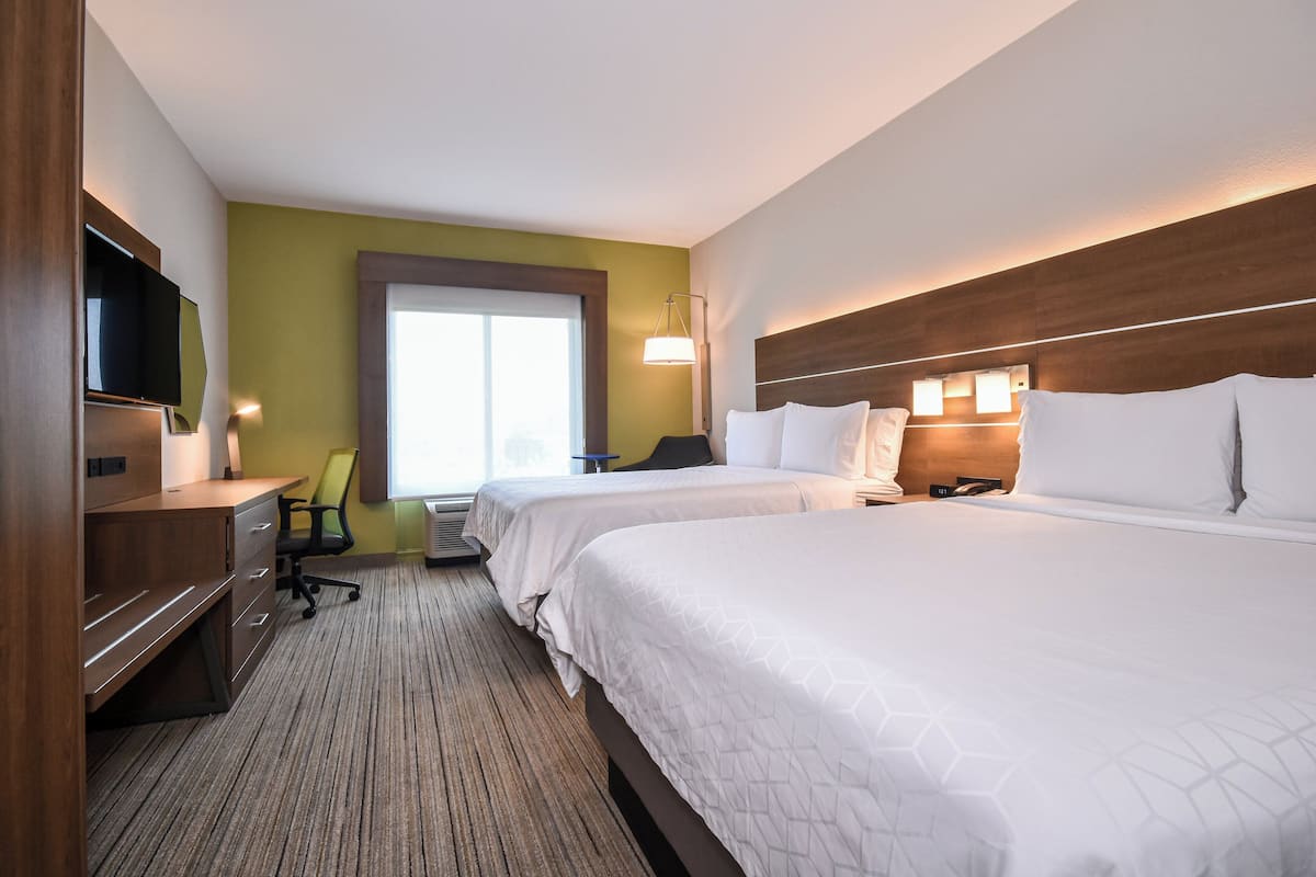 Une chambre d’hôtel avec deux lits, un bureau avec une chaise, une télévision et une fenêtre avec des stores.