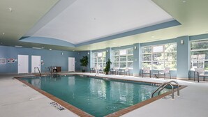 Una piscina interior con agua cristalina, rodeada de sillas de descanso y plantas en macetas.
