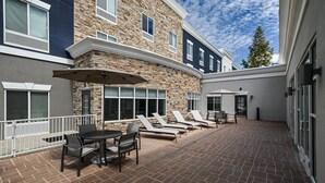 Un patio con mobiliario exterior, un muro de piedra y cielo despejado.