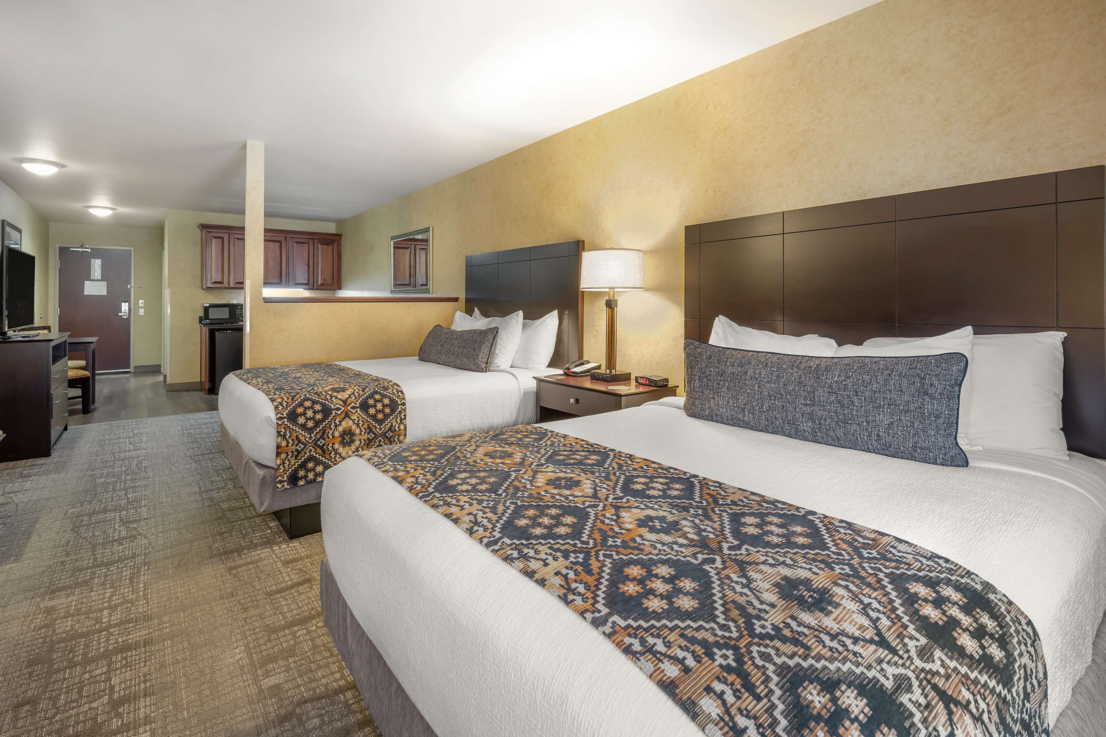 A hotel room with two beds, a kitchenette, and a bathroom.