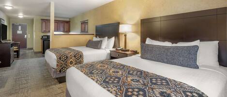 A hotel room with two beds, a kitchenette, and a bathroom.
