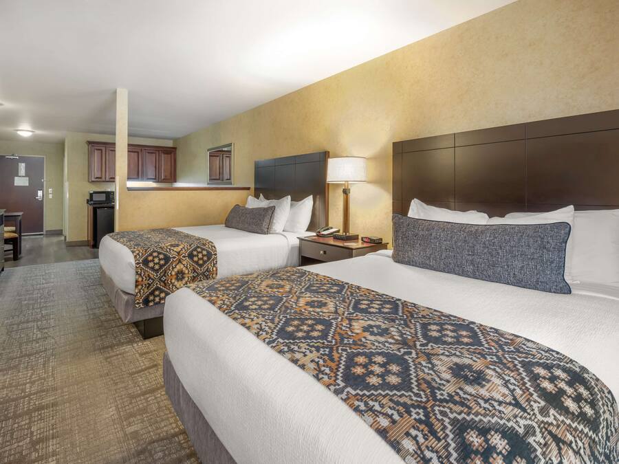 A hotel room with two beds, a kitchenette, and a bathroom.
