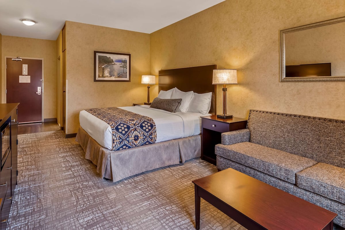 A hotel room with a bed, a sofa, a desk, and a lamp.