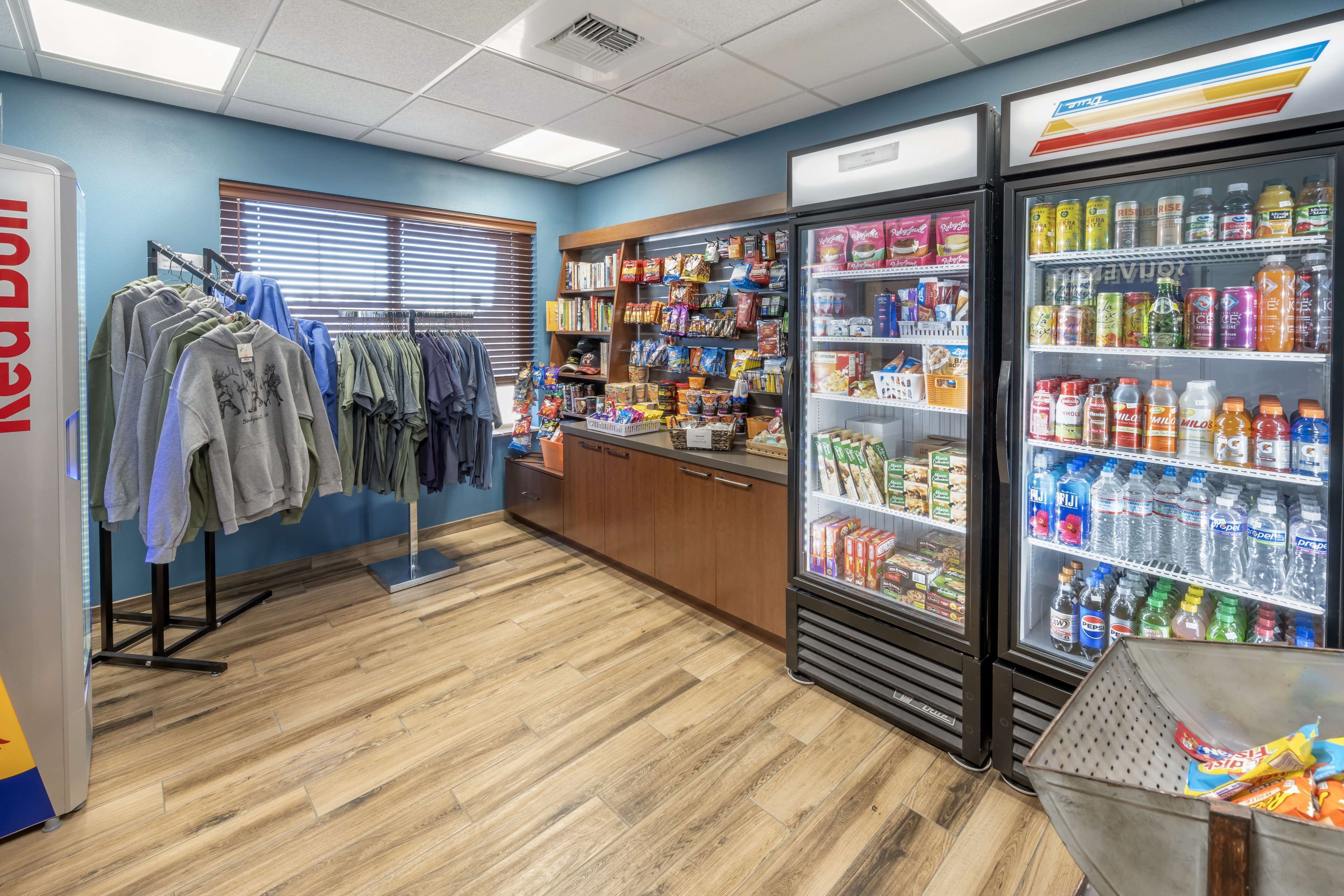A store with clothing racks, shelves stocked with snacks, and refrigerated beverage cases.