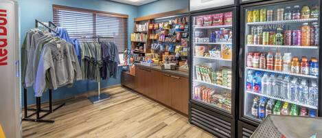 A store with clothing racks, shelves stocked with snacks, and refrigerated beverage cases.