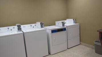 A laundry area with four Whirlpool washers and dryers, a trash can, and a wooden counter.