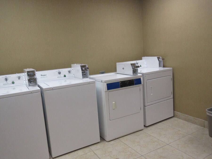 A laundry area with four Whirlpool washers and dryers, a trash can, and a wooden counter.