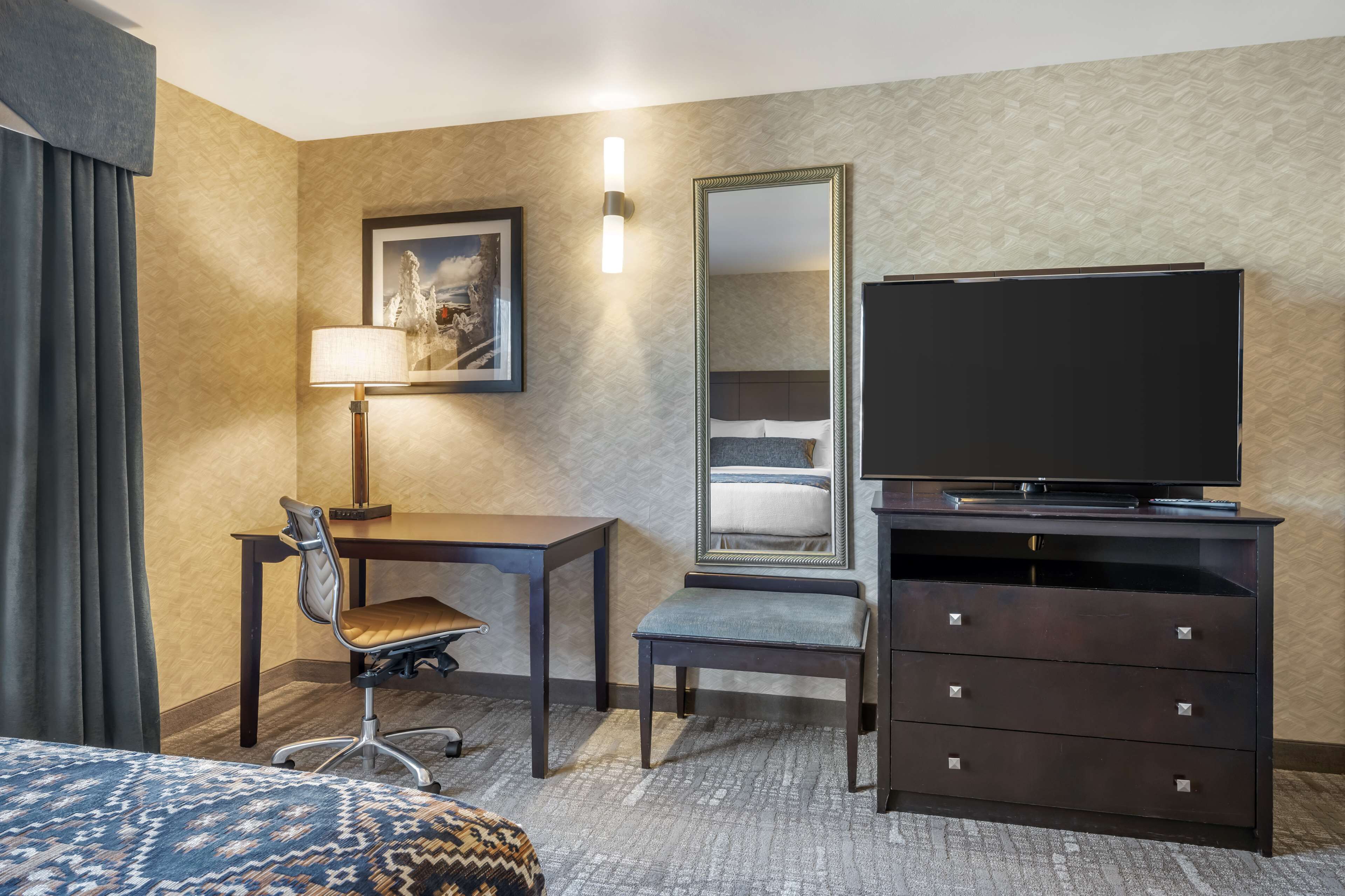 Une chambre d’hôtel comprenant un lit, un bureau avec une chaise, un téléviseur posé sur une commode, un miroir et une lampe.