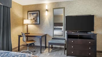 A hotel room with a bed, a desk with a chair, a television on a dresser, a mirror, and a lamp.